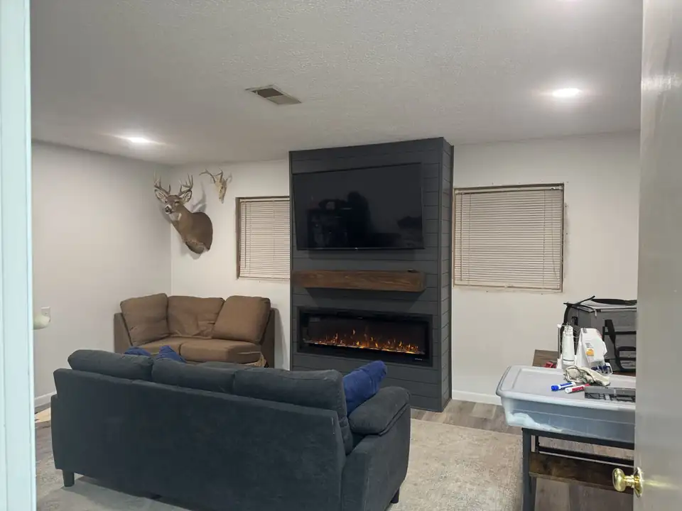 Home remodeling project: charcoal shiplap fireplace wall with a linear electric fireplace, stained wood beam mantel and TV above, built by Oak Lane Remodeling